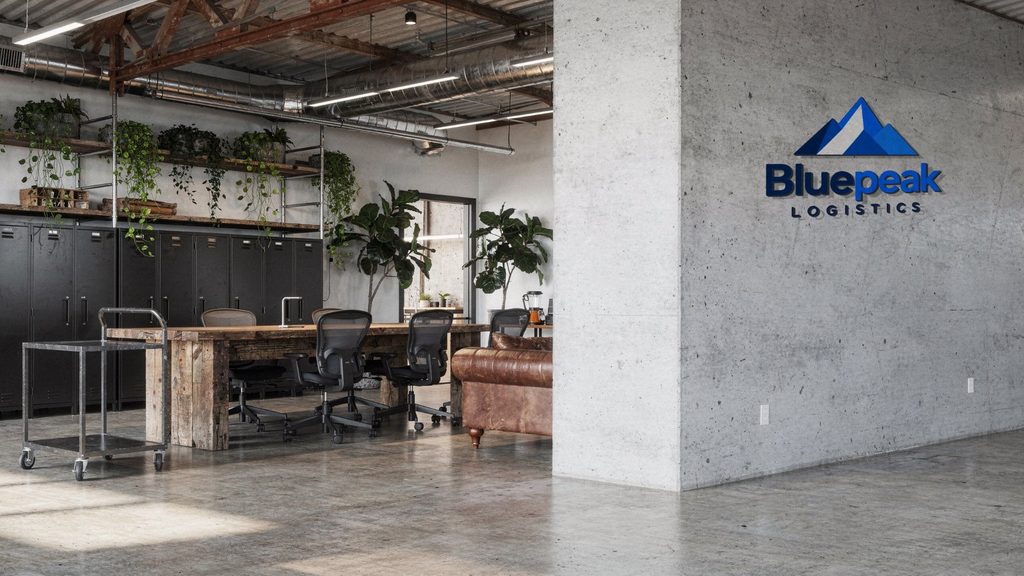 A woman on a video call in front of an office wall with the Bluepeak Logistics logo